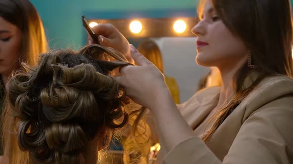 Hairdresser with Hairbrush and Makeup Artist Doing Hairstyle and Makeup to Young Woman