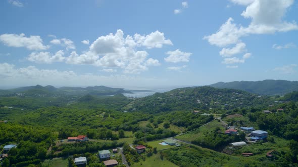 Aerial of few houses on green rural landscape overlooking sea