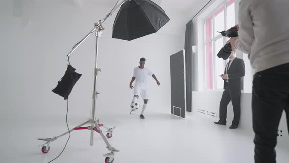 Afroamerican Footballer is Posing for Camera of Photographer in Studio Showing Kickup Skill