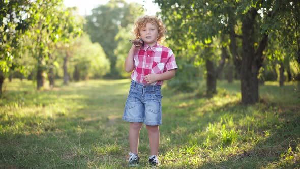 Wide Shot Portrait of Cute Redhead Curlyhaired Little Boy with Ukulele Posing in Sunny Summer Spring