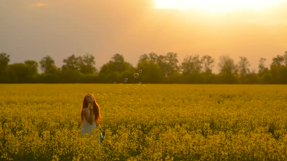 Young Redhair Woman Blowing Bubbles at the Camera Outdoors in Summer Meadow