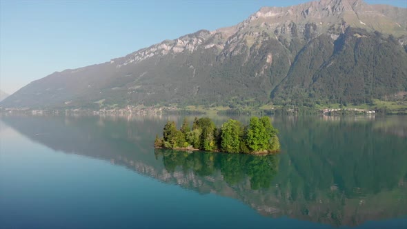 Droneshot of little island in Switzerland with mountain panorama in the back. Early morning light wi