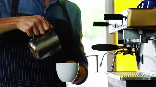 Waiter pouring milk in coffee at counter