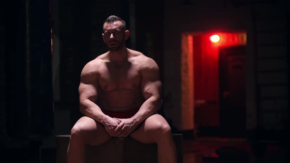 Tough Big Man Sitting in the Gym with Red Contrast Lighting