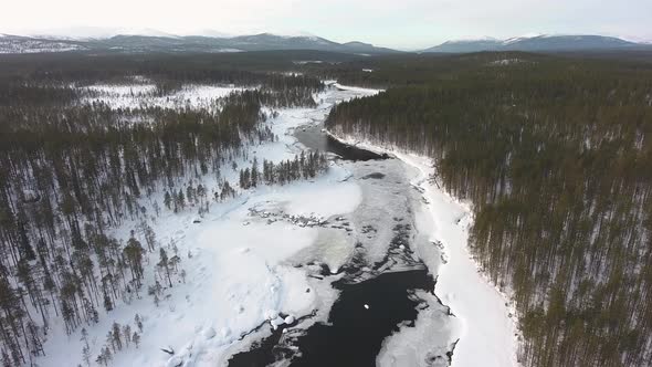 Flight over a frozen river and winter snowy forest