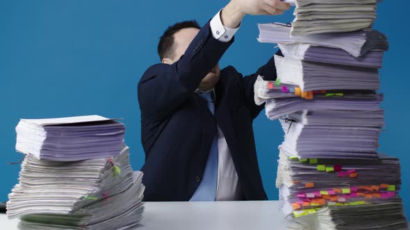 Stressed Accountant Manager Takes Stack of Unfinished Documents From Large Pile