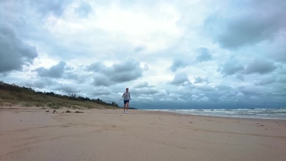 Man is running in the beach in the morning. Windy morning, wavy sea, blue water, cloudy, near storm.