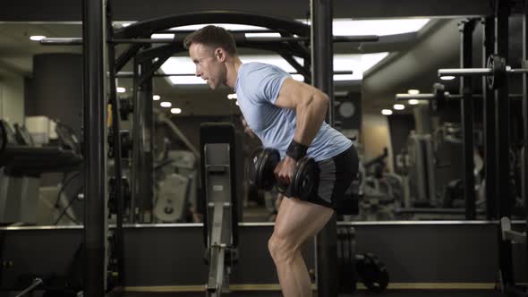 Muscular man pulling heavy dumbbell at the gym.