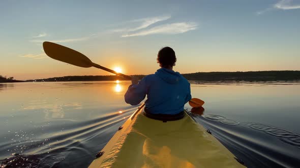 Guy Sails Kayak Along River Water Against Island at Sunset