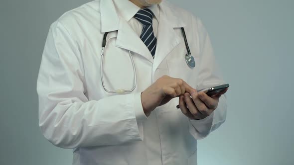 Male Doctor Typing Message on Modern Smartphone, Using Smart Gadget for Work