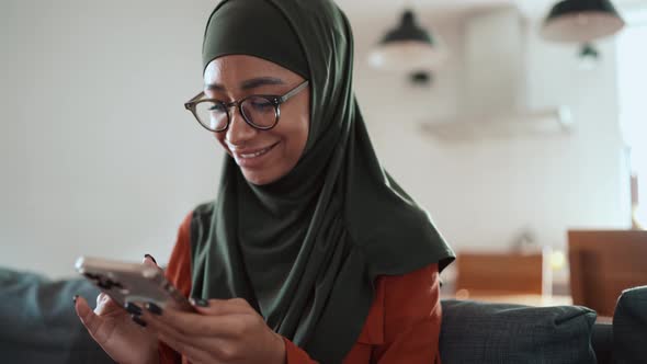 Smiling Muslim woman wearing eyeglasses texting by phone