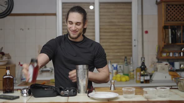 Playful Young Male Playing Around with Agave Syrup Bottle and Using Jigger to Put on Cocktail Shaker