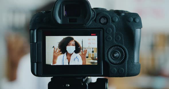 Black-Skinned Female Medic in Facial Mask which Streaming on Camera from Medical Office