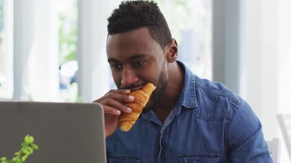 African american businessman using laptop and eating croissant in cafe