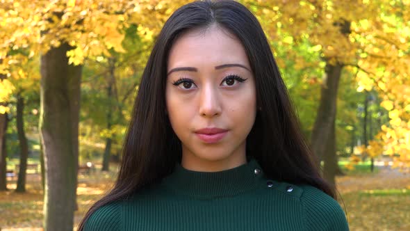 A Young Asian Woman Looks Seriously at The Camera in A Park