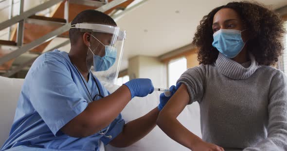 African american female doctor wearing face mask vaccinating african american patient