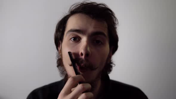 Young Man is Combing His Beard Looking at Camera Filmed Isolated on White Background