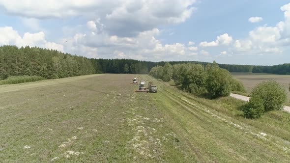 Aerial view of two Combines harvesting and trucks on grass field. 44