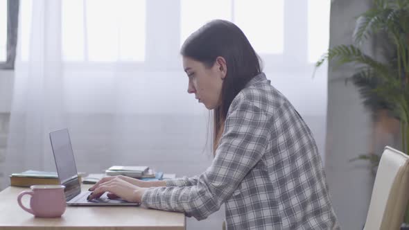 Side View of Young Caucasian Girl Typing Fast on Laptop Keyboard. Serious Female Freelancer Working