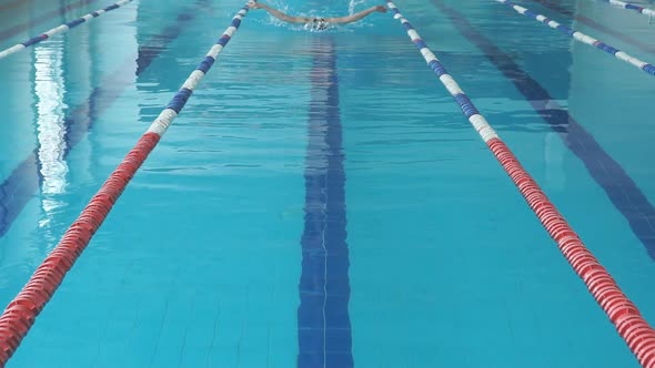 Young Woman in Goggles and Cap Swimming Butterfly Stroke Style in the Blue Water Indoor Race Pool