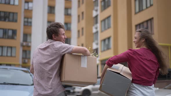 Tracking Shot Happy Couple Walking in Slow Motion on Parking Lot with Cardboard Boxes Talking