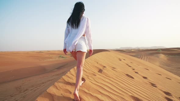 Rear View Young Woman Walking on Sandy Mountain in Desert with Her Arms Outstretched