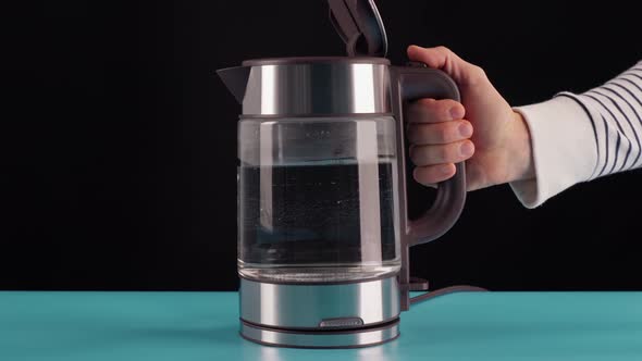 The Hand Takes a Glass Electric Kettle for Boiling Water for Drinks Tea or Coffee