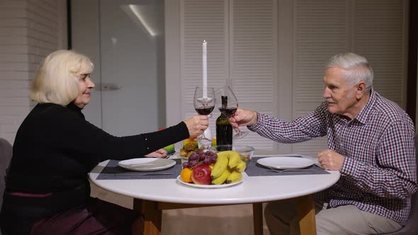 Senior Relaxed Couple Eating Dinner and Drinking Glasses of Red Wine Together in the Kitchen at Home