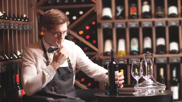 Elegant Young Sommelier with Bow Tie Uncorking Bottle of Wine in Wine Boutique.