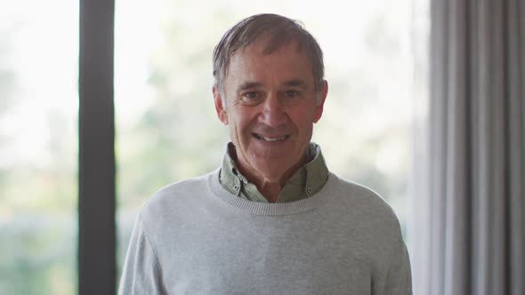 Portrait of happy senior caucasian man in living room smiling to camera