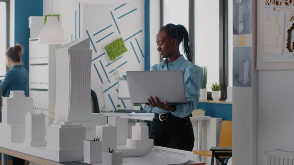 Woman Architect Holding Laptop to Analyze Building Model in Architectural Office