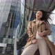 A Girl in a Brown Coat Stands Against the Backdrop of a Tall Building - VideoHive Item for Sale
