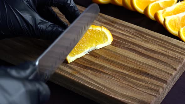 Man Slicing Raw Orange with Kitchen Knife on Wooden Cutting Board