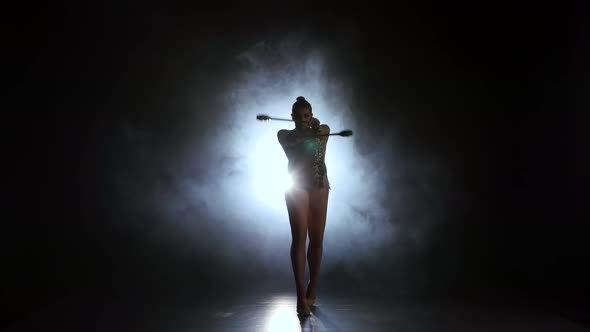 Rhythmic Gymnast Throws Mace Up and Catches Her. Black Background. Light Rear. Silhouette