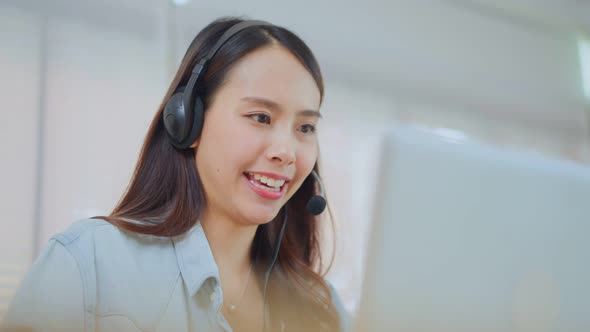 Asian attractive telemarketing or call center with headset work and talk on computer lap top at home