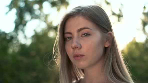 Beautiful Blonde Young Woman in the Summer Garden Looking at Camera at Sunset