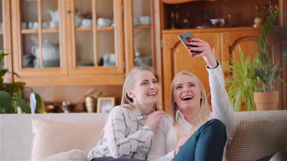 Two Positive Energetic Women Taking Selfie Photo on a Sofa in Luxury Modern Living Room