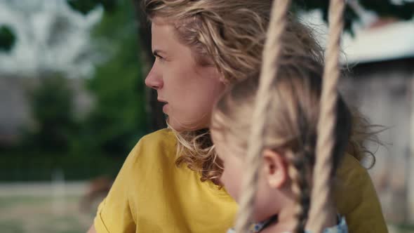 Close up of mom with little girl swinging and talking together in summer day