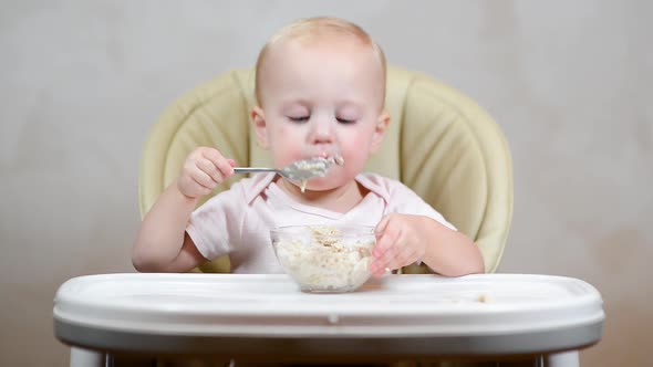 little girl ineptly eats porridge in a feeding chair