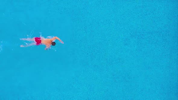 Aerial View of Man in Red Shorts Swims in the Pool. Slow Motion