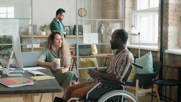 Afro Man with Disability Talking with Female Colleague over Coffee in Office