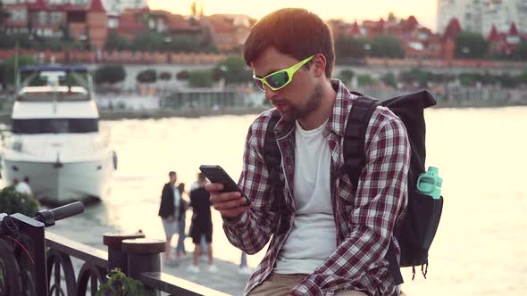 Male Use Phone Surfing Internet Online Shopping at Smartphone Outside in Summer on River Embankment