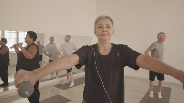 Mature Asian Woman Exercising with Dumbbells at Group Fitness Class