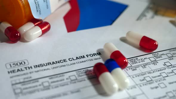 Prescription drug bottle and pills spilling onto a patient health insurance claim form.