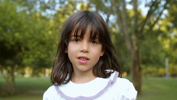 Pensive Cute Little Black Haired Girl Standing in City Park