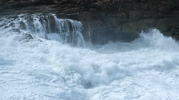 Wave crash into rocks, frothing sea water streams down rock-face, turbulent ocean