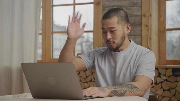 Asian Man Greeting on a Video Call Using Laptop Indoors