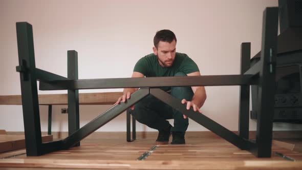 Man Attaching Metal Legs Of A Wooden Table - wide shot