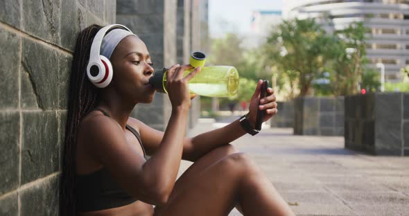 African american woman exercising outdoors drinking water and using smartphone in the city