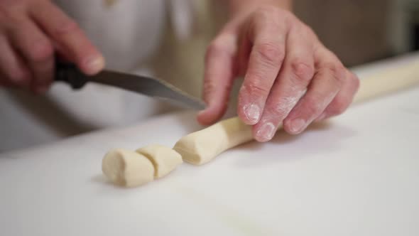 Female Hands Cut the Dough Twisted Into a Sausage on the Table Into Small Pieces